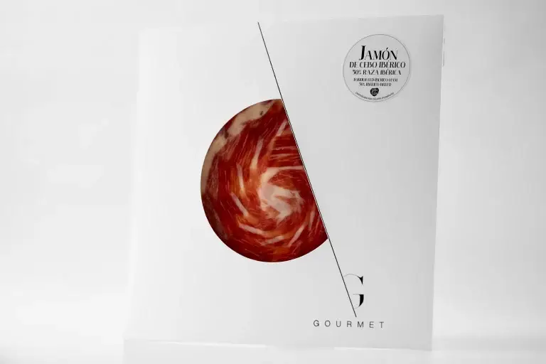 Guijuelo Gourmet Jamón de Cebo 50% Ibérico, en un elegante sobre cuadrado blanco, con una ventana circular en el centro que permite ver el producto. En la esquina superior derecha, lleva una etiqueta blanca.