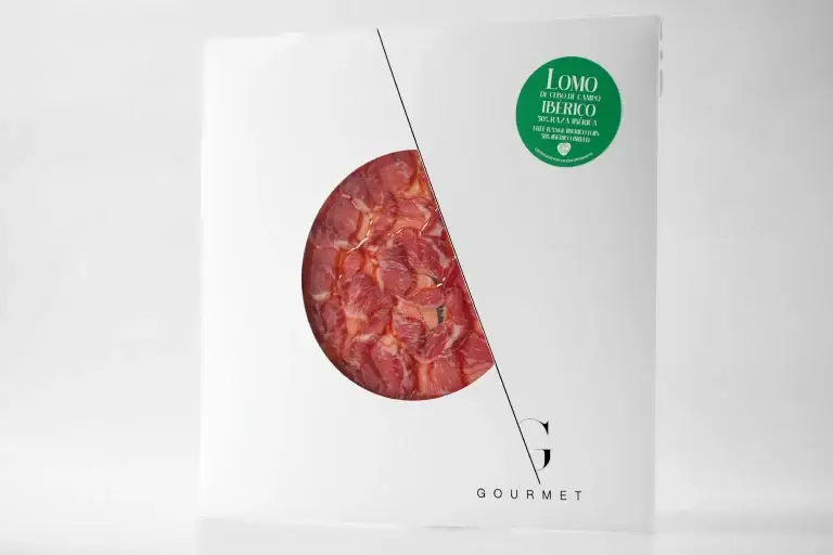 Lomo de Cebo de Campo 50% Ibérica Guijuelo Gourmet en un envoltorio de papel blanco en forma de sobre cuadrado, con un diseño de círculo en el centro y una etiqueta verde pegada en la esquina superior derecha.