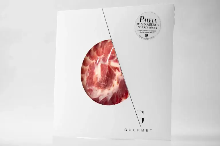Guijuelo Gourmet Paleta de Cebo 50% Ibérica en un empaque blanco cuadrado, con una ventana circular en el centro que permite ver el color de la carne. En la esquina superior derecha, una etiqueta blanca con información del producto.