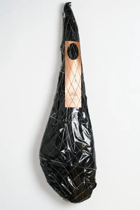 Jamón de bellota 100% ibérico entero, presentado en un saco de tela negra con una red blanca dispersa en el exterior. El saco lleva impreso un logo blanco y cuenta con una etiqueta dorada de papel que resalta su calidad premium.