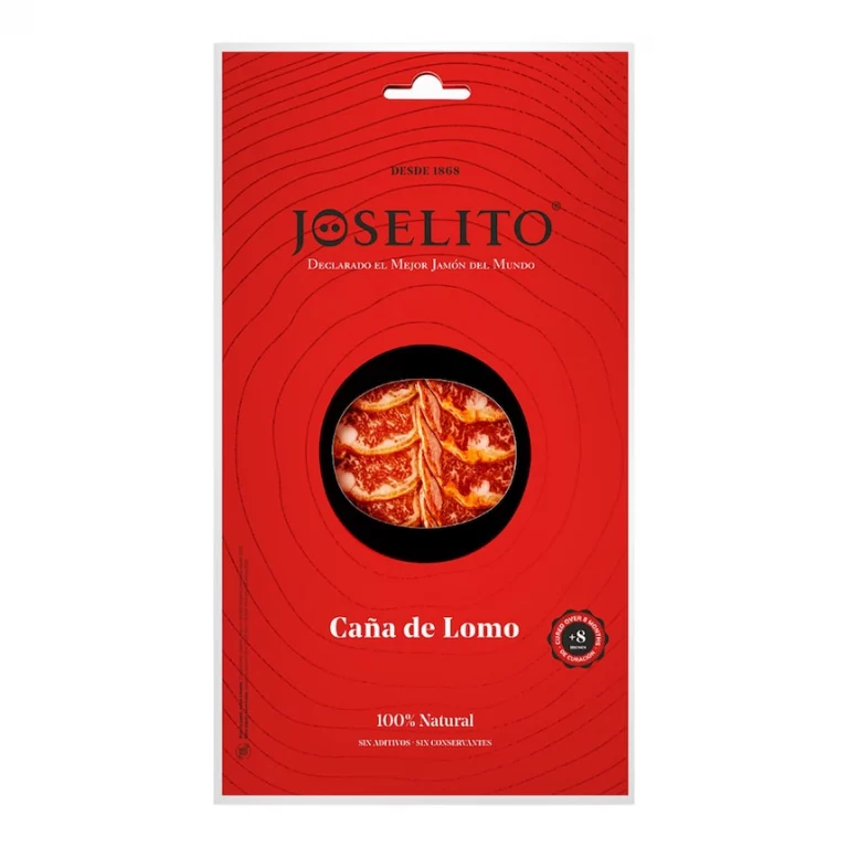 Un sobre rojo con un corte circular en el centro, mostrando caña de lomo Joselito loncheado envasada al vacío, con rodajas de color rojo intenso y un atractivo veteado de grasa, resaltando su textura jugosa y sabor delicado.
