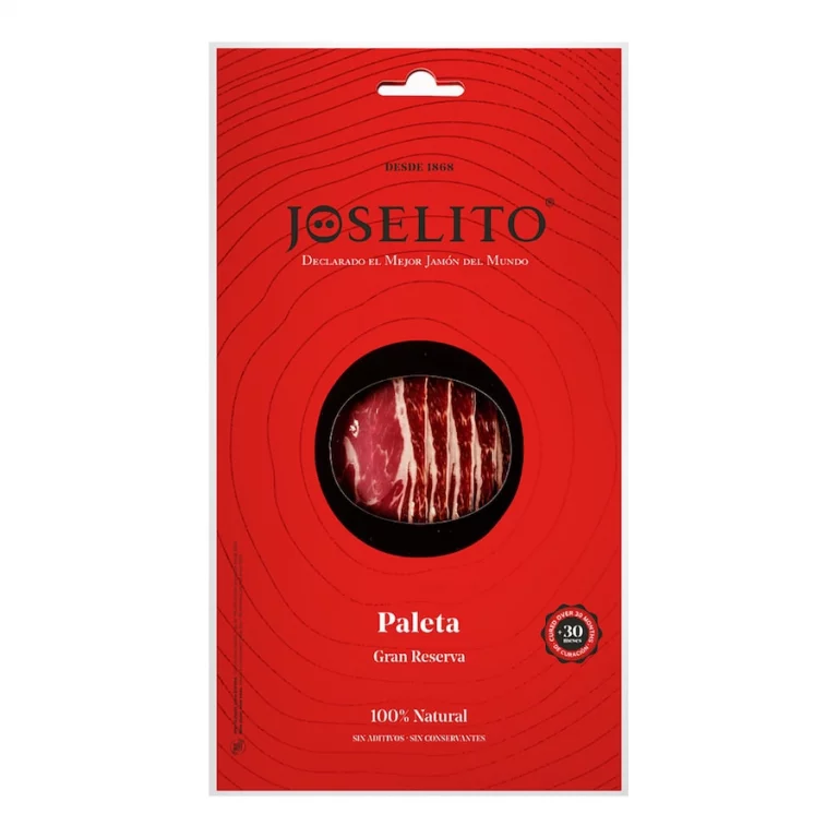 Un sobre rojo con un corte circular en el centro, revelando un trozo de jamón ibérico Joselito Paleta Gran Reserva envasado al vacío, con un color rojo oscuro y vetas de grasa blanca, resaltando su textura jugosa.