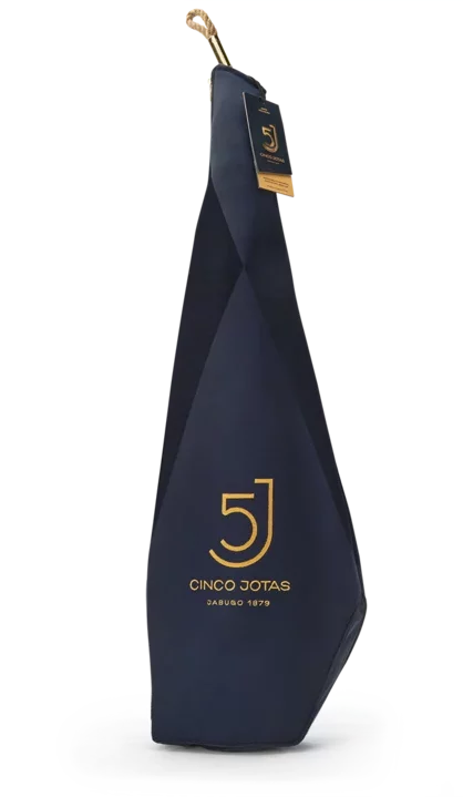 Una pata entera de jamón Cinco Jotas, que pesa entre 7 y 8 kg, envuelta en una bolsa de tela azul oscuro con un diseño de logo amarillo.
