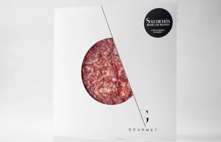 Paquete cuadrado blanco con un círculo transparente en el centro, mostrando el salchichón ibérico extra en su interior, y con una etiqueta negra en la esquina superior derecha.