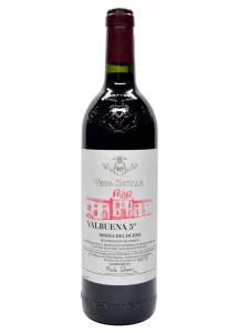 Botella de vino tinto, con cápsula de color rojo oscuro, cuerpo de botella color negro. La etiqueta en la botella es de color blanco, escrito valbuena 5 2020. Denominación de origen en Ribera de Duero.